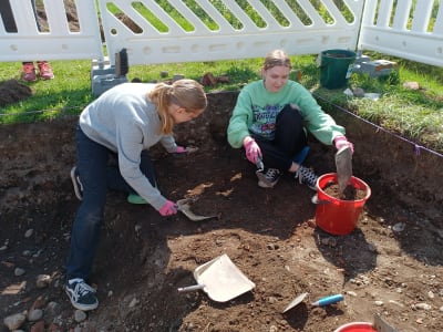 Två flickor hanterar med hink och skyffel i en utgrävningsgrop