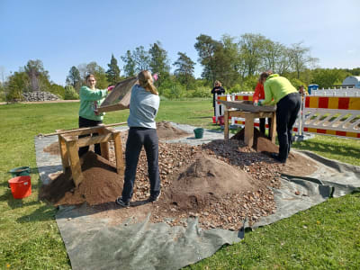 Fyra personer sållar fram fynd på ett utgrävningsområde