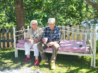 Ett äldre par i en soffa ute i en trädgård. 