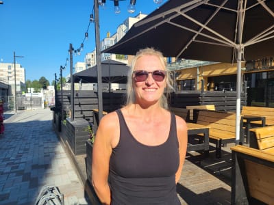 En kvinna i solglasögon står på en gågata.