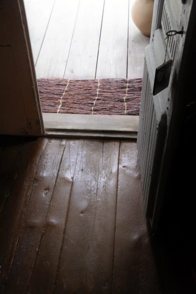 Tröskeln till husets ingång med slitage i trägolvet efter långt bruk.