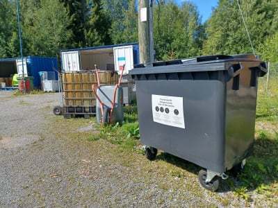 En grå låda på hjul för insamling av textilier på en återvinningsstation