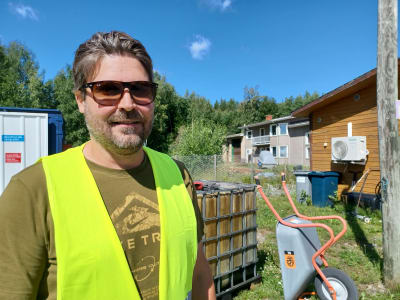 En ung man i solglasögon och en gul arbetsväst står på en återvinningscentral