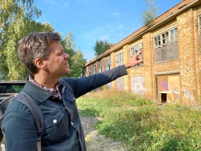 En man (Vasa stads planläggningsarkitekt Oliver Schulte-Tigges) pekar med fingret på den gamla tvålfabriken, en tegelbyggnad som liknar en ruin.