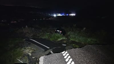 En bil ligger i diket och en asfalterad väg ligger i bitar på ett gräsområde i mörkret.