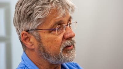 En medelålders man med grått hår och skägg och glasögon.