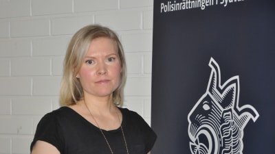 Ädre kriminalkonstapel Sara Malm står vid en banderoll med polisens lejonemblem.