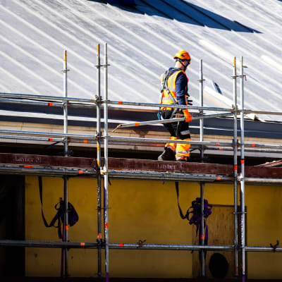 En byggnadsarbetare går på en ställning vid ett tak.
