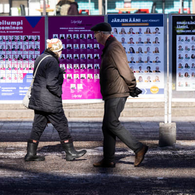 Två personer går förbi plakat med valreklamer.