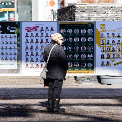 En kvinna står på en gata framför ett antal valreklam.