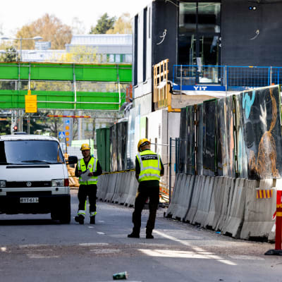 Byggarbetsplats runt och över en väg. Två män i arbetskläder och skyddshjälmar syns i bild.