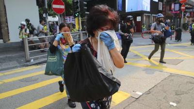 Förbipasserande försöker skydda sig mot tårgasen under söndagens demonstration i centrum av Hongkong.
