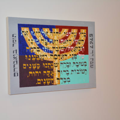 En tavla av en sjuarmad ljusstake. Texten är en bön för förmögenhet på hebreiska.