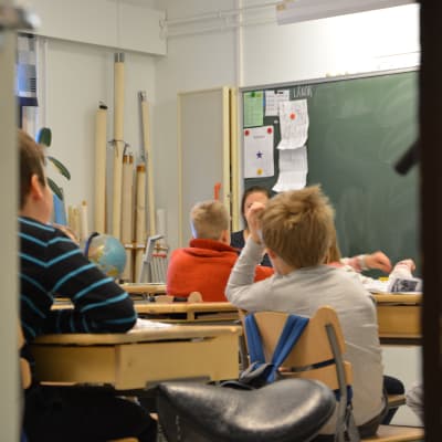 Barn sitter med ryggarna åt kameran i ett klassrum