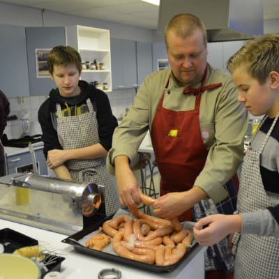 Kökschef Kenneth Löfberg instruerar högstadieeleverna Tomi Berg och Emil Lindholm i korvstoppningens ädla konst.