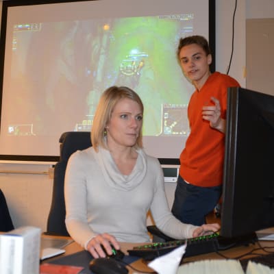 Linda Mannila spelar datorspel och David Mannström förklarar hur spelet går till.