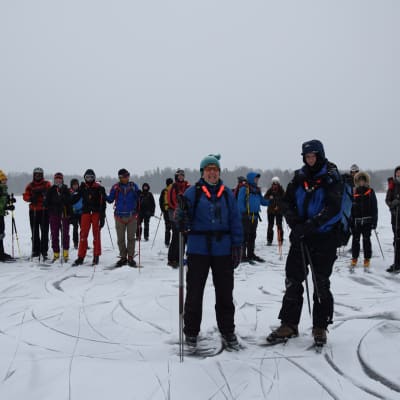 En instruktör och en långfärdsskrinnare står framför en grupp långfärdsskridskoåkare på isen.