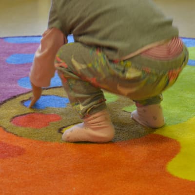 Ett litet barn leker på en färggrann matta.