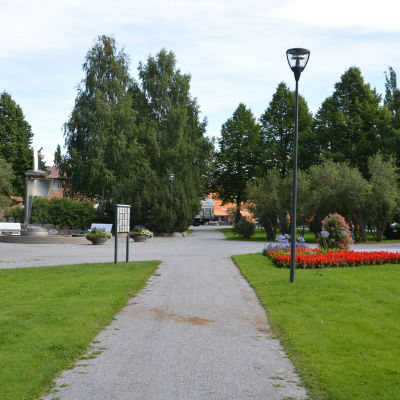 En somrig bild av Brändö torg med blomrabatter till höger och en fontän till vänster.