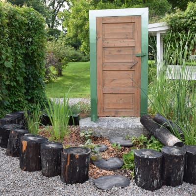 Trädgårdsrabatt med sumpmarksväxter och en fristående dörr i mitten