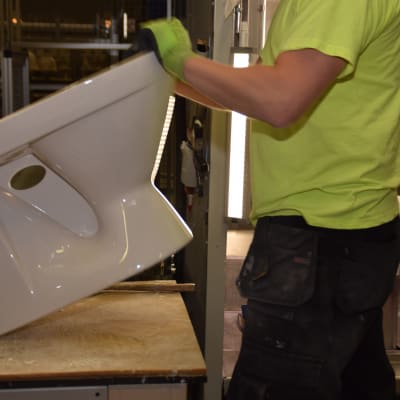 En arbetare på Ido badrums fabrik i Ekenäs granskar med sina händer att wc-stolen är hel.