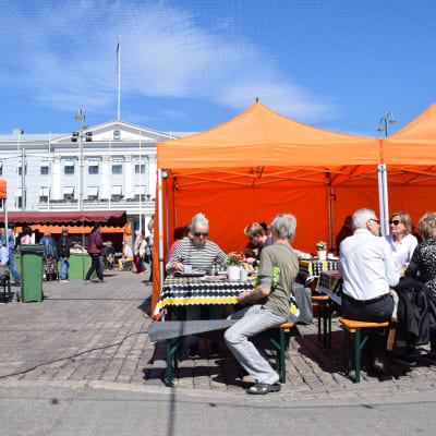 Folk sitter och dricker kaffe vid torgcafét på Salutorget. I bakgrunden syns stadshuset.