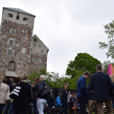 Människor minglar framför försäljningsstånd under businessfestivalen The Shift, Åbo slott i bakgrunden.