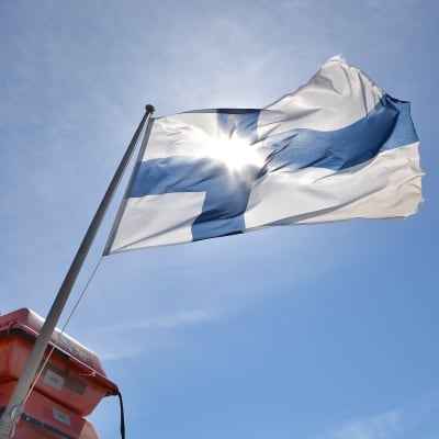Solen skiner genom Finlands flagga som vajar på motorbåt.