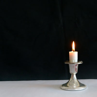 Kort, vitt stearinljus brinner i en liten ljusstake.