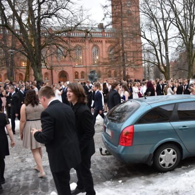 Niondeklassister i festkläder står utanför Vasa stadshus efter att byggnaden tvingades evakueras. Flera hundra personer står på gatan och i parken.