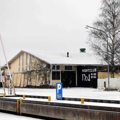 En gul gammal magasinbyggnad i Ekenäs norra hamn. På ena sidan syns en björk. Marken är täckt av snö.