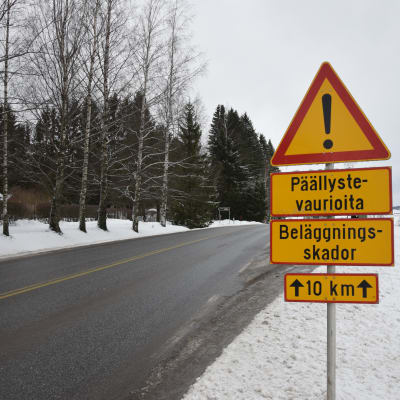 En skylt som varnar för beläggningsskador vid kanten av en vintrig väg.