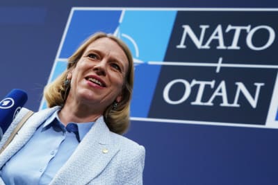 En leende Anniken Huitfeldt klädd i ljusblått. Bakom henne syns Natos logotyp.