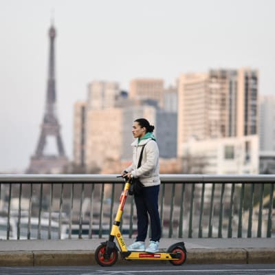 Mies ajaa sähköpotkulaudalla sillalla Pariisissa.