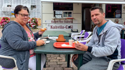 En kvinna och en man sitter vid ett bord på Lovisa torg. De har varsin munk i handen.