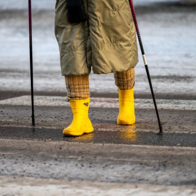 En person i gula stövlar går över ett övrgångställe. Det är is och halt.