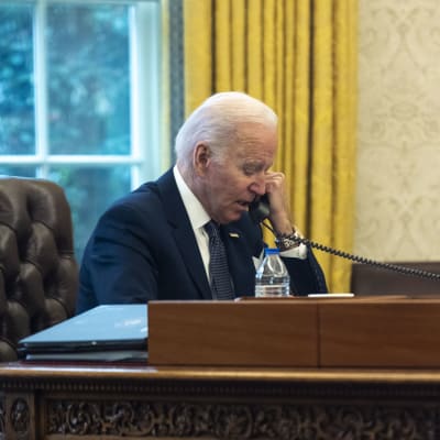 Joe Biden sitter i sitt kontor vid ett skrivbord och talar i telefon.