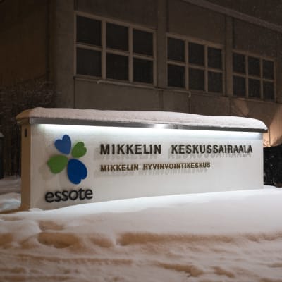 Mikkelin keskussairaalan julkisivu. Edustalla keskussairaalasta ja hyvinvointikeskuksesta kyltti.