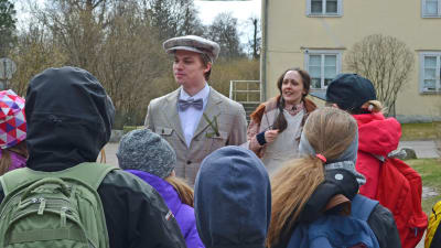 Edvin Eliasson (Elias Edström) tilltalar en barnaskara framför Hertonäs gård, med en piga i bakgrunden.