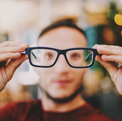 en blurrad man som håller ett par glasögon framför sig.