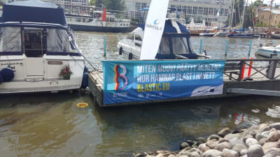 En havssoptunna finns i Åbo gästhamn, med en stor banderoll invid: Hur hamnar plast i vattnet?