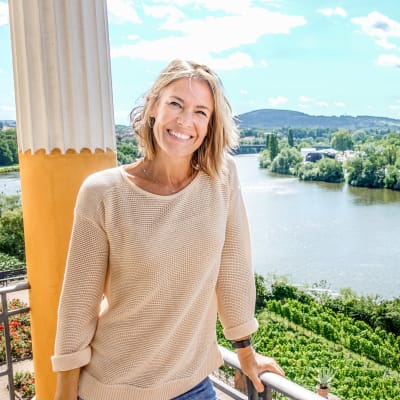 Ella Kanninen hymyilevänä aurinkoisella parvekkeella Pohjois-Italiassa. Ohjelma on Ellan matkassa: roomalaisten jäljillä.