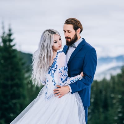Ett brudpar poserar utomhus, brudgummen har blå kostym och bruden blå detaljer i sin vita klänning.