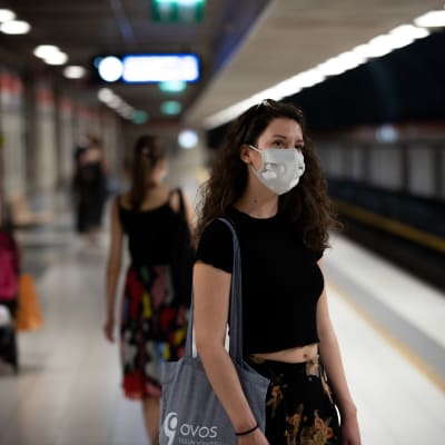 En kvinna som väntar på metron vid perrongen och bär munskydd.