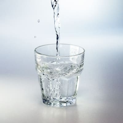 Vatten som rinner i ett glas mot en neutral vit bakgrund.