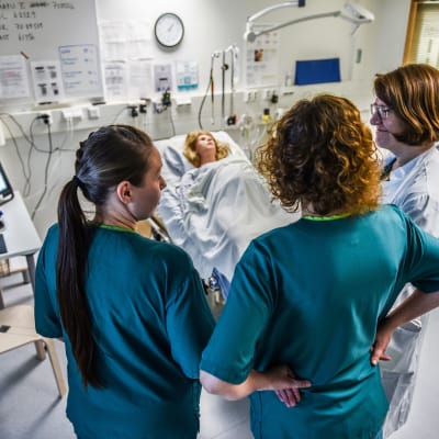 Tre sjukvårdare tittar på en patientsäng.