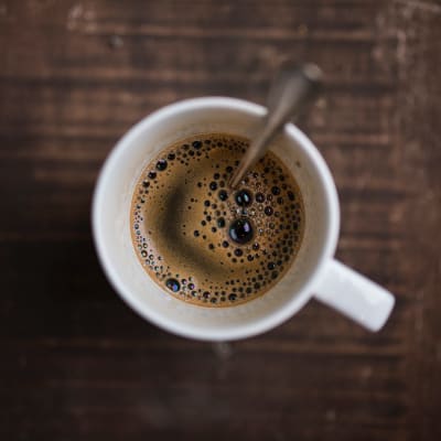 En mugg svart kaffe med en sked i.