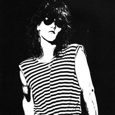 En svartvit bild på Jan "Nasty Suicide" Stenfors där han står med solglasögon på och med tummarna i fickorna.