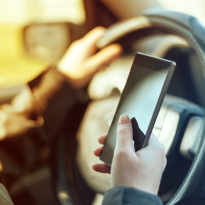 En person knappar på en smarttelefon i förarsätet på en bil.