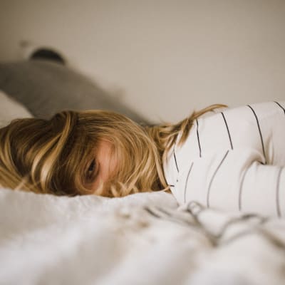 nainen makaa sängyllä ja katsoo kameraan hiuksien takaa